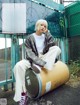 A woman sitting on top of a barrel in front of a fence.