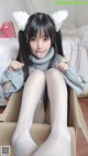 A girl in a gray sweater and white tights sitting in a cardboard box.