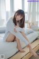 A woman sitting on top of a bed in a white shirt.