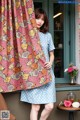 A woman standing in front of a window holding a pink and blue floral curtain.