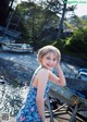 A young girl in a blue dress standing by the water.